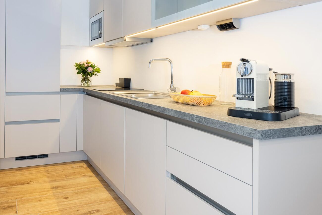 Close-up einer Küche in hellgrau mit indirekter Beleuchtung. Kaffeemaschine und Obstkorb im Vordergrund.